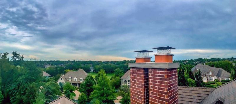 A brick chimney with two capped flues above a neighborhood