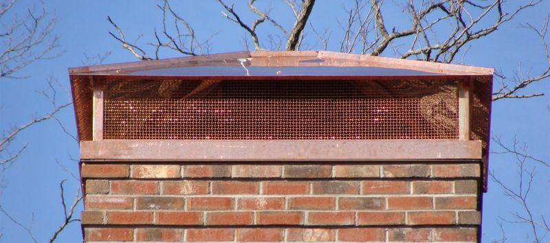 A copper cap with a mesh screen on a brick chimney