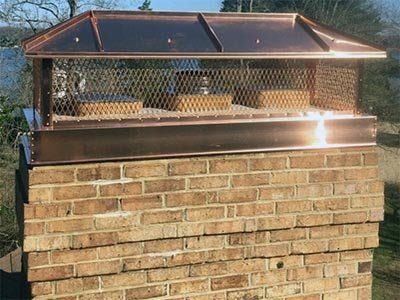 A copper cap with mesh sides on a brick chimney