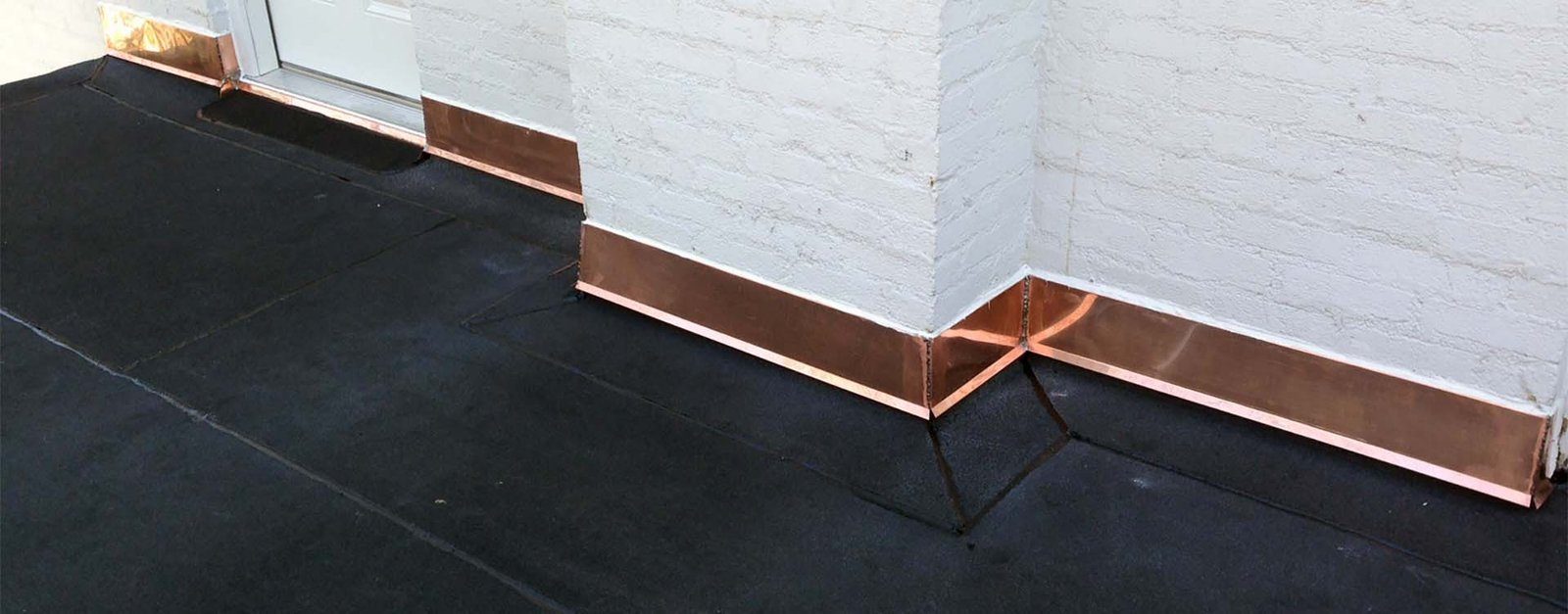 Copper flashing where a flat roof meets a white brick wall