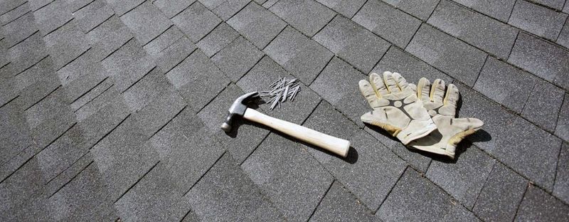 A hammer, nails and work gloves on a shingle roof