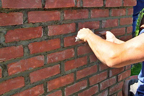 Pressing new mortar into brick joints by hand