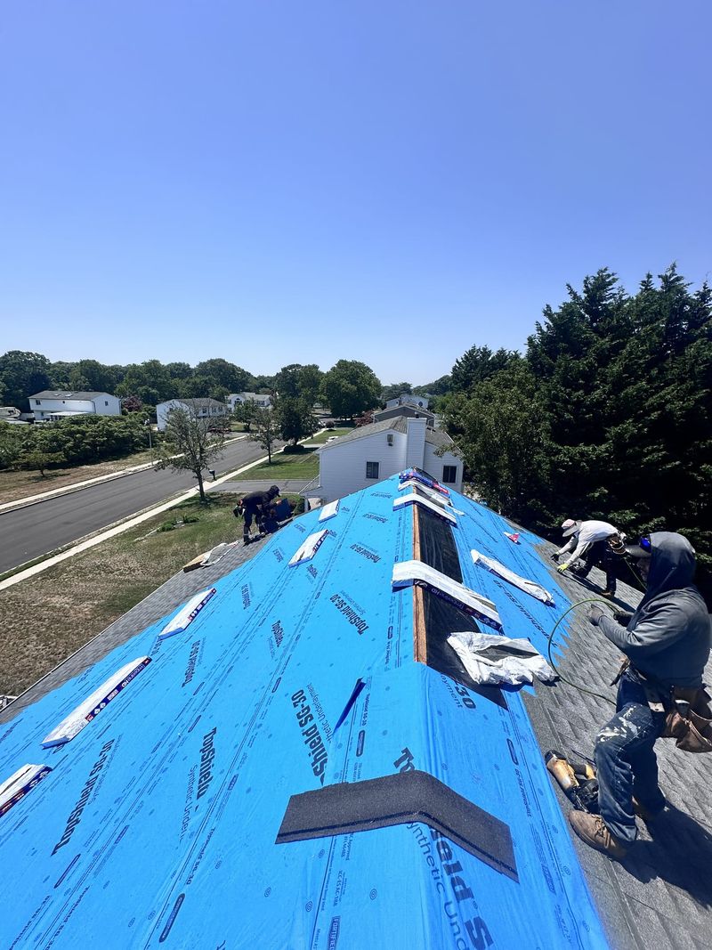 The crew re-roofing a house, seen from the ridge, with underlayment down and shingles going on