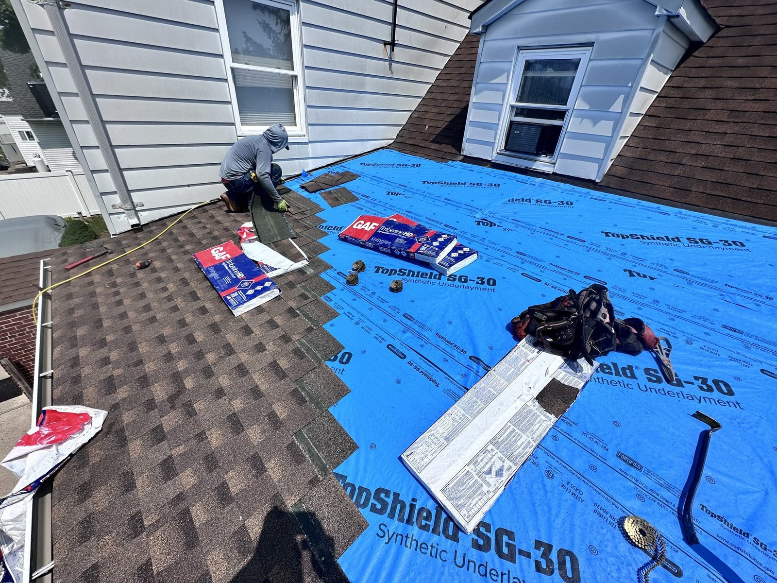 One of the crew laying new shingles over underlayment beside a dormer